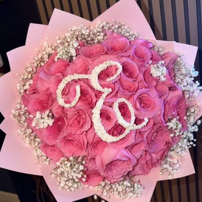Coral garden-rose bouquet with a script monogram initial picked out in white blooms, wrapped in blush paper