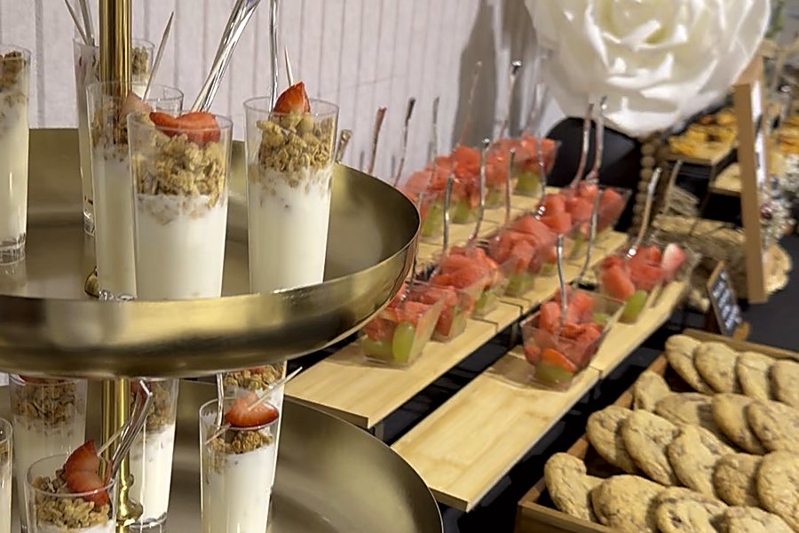 Tiered dessert station with strawberry parfait cups, fruit skewers and cookies on gold stands