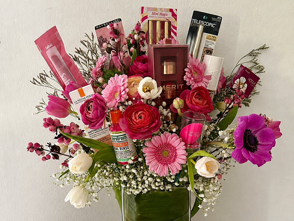 Tall bouquet of ranunculus, gerbera daisies, tulips and anemones arranged with boxed makeup and skincare products