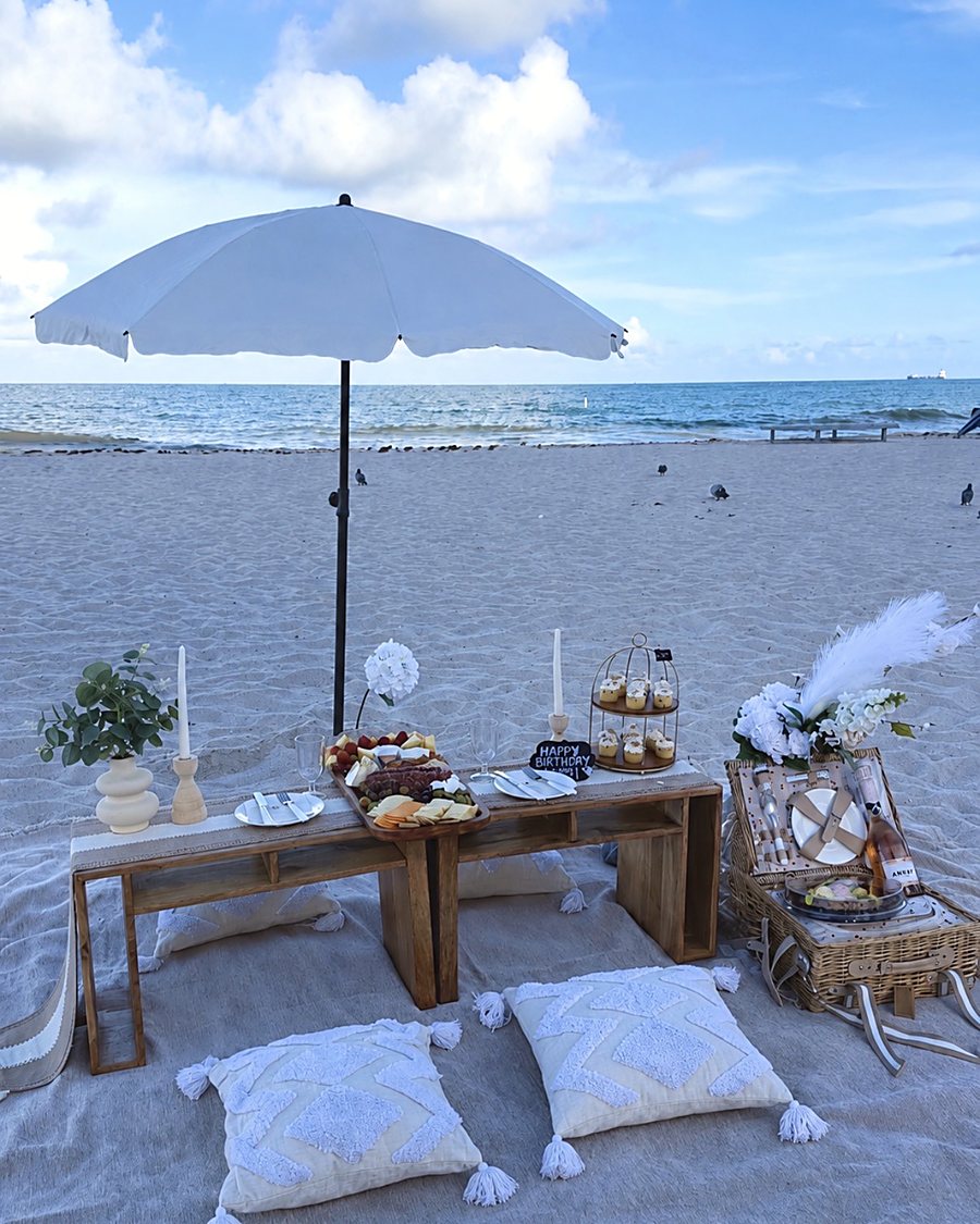 Beach picnic set for two under a white umbrella with a low wooden table and a grazing board