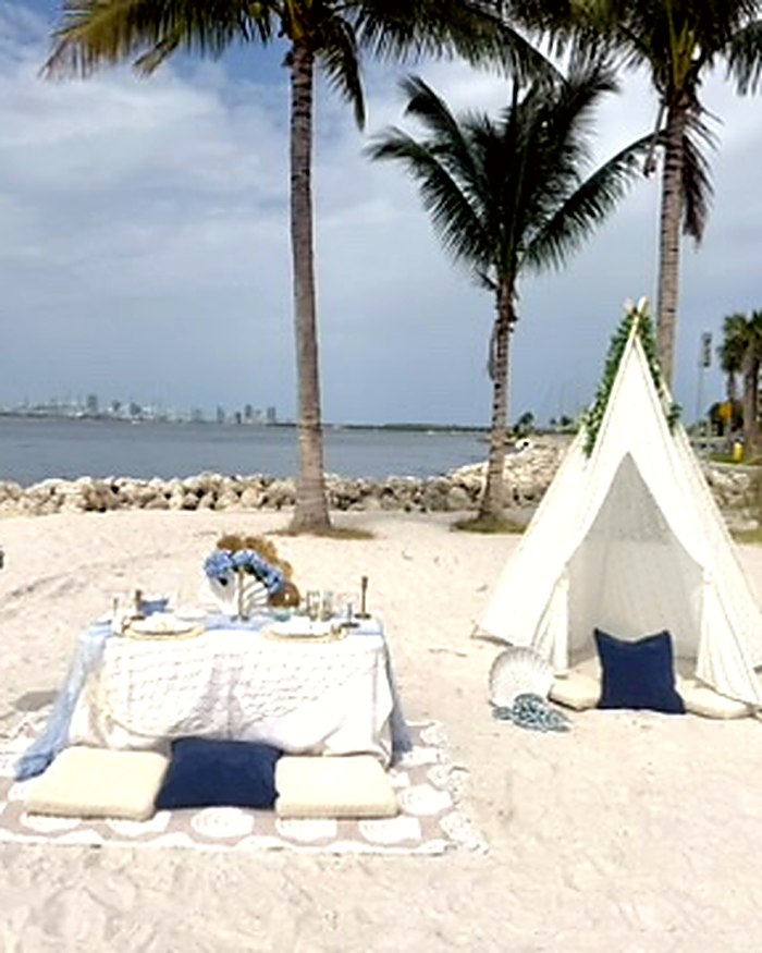 Styled beach picnic with a linen teepee and low table on the sand in Miami