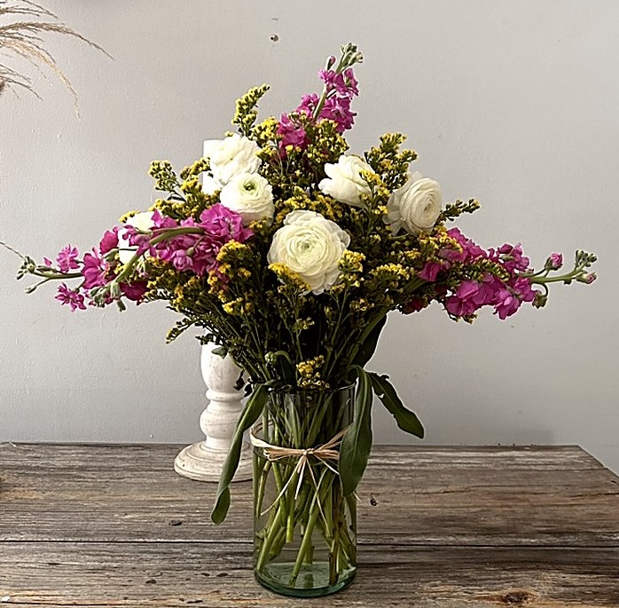 Bouquet of white ranunculus and pink stock in a glass vase on a wooden table
